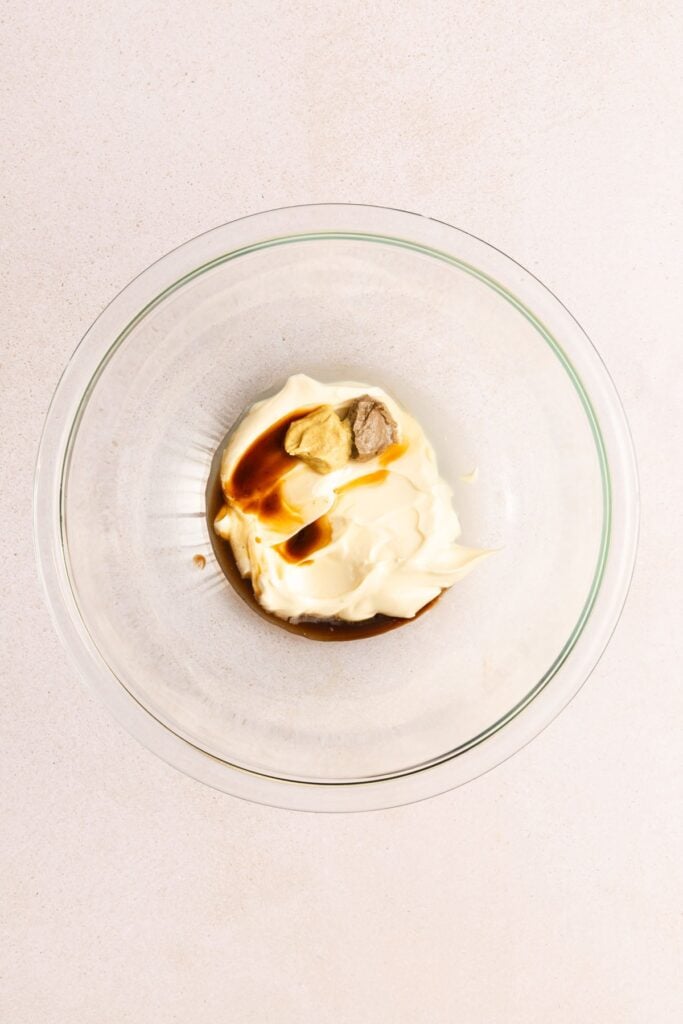 A glass bowl containing mayonnaise, mustard, and Worcestershire sauce on a light-colored surface.