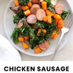 A plate of sliced chicken sausage, kale, roasted sweet potatoes, and red onions, with a fork on the side. Text reads "Chicken Sausage Sheet Pan Meal.