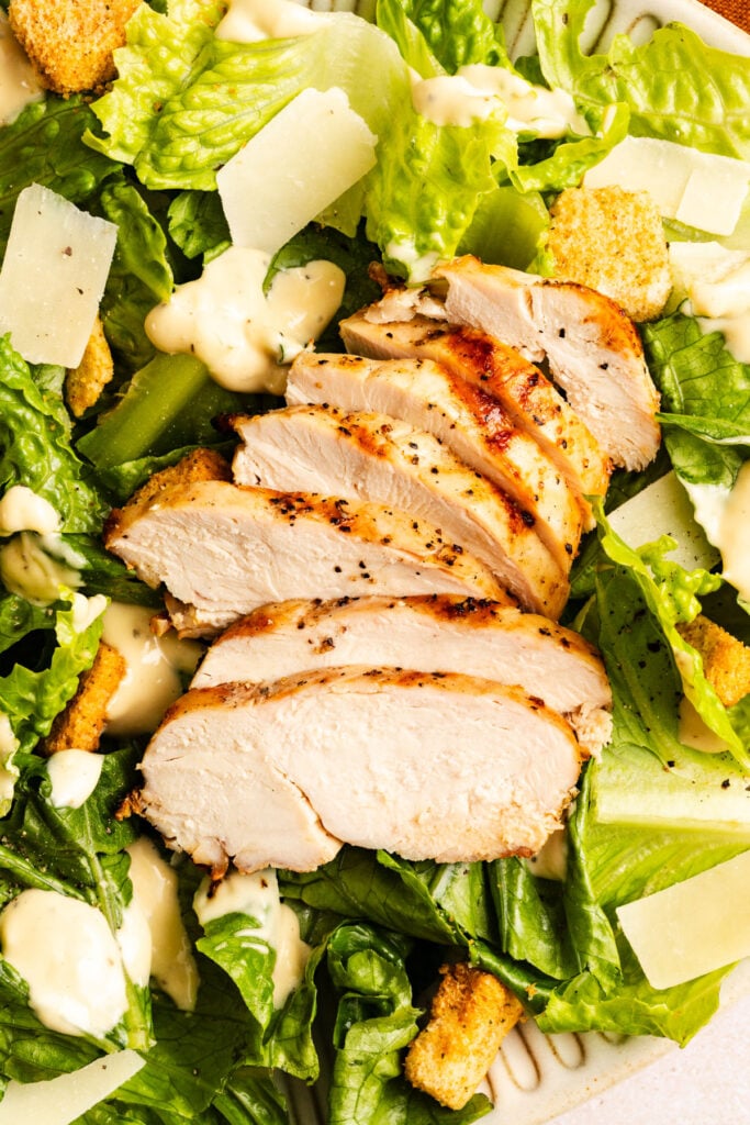 Sliced grilled chicken breast on a bed of romaine lettuce with croutons, shaved parmesan, and Caesar dressing.