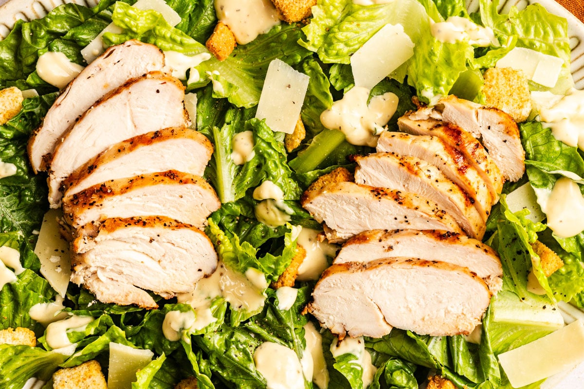 Sliced grilled chicken breast on a bed of lettuce, topped with croutons, shaved parmesan, and Caesar dressing.