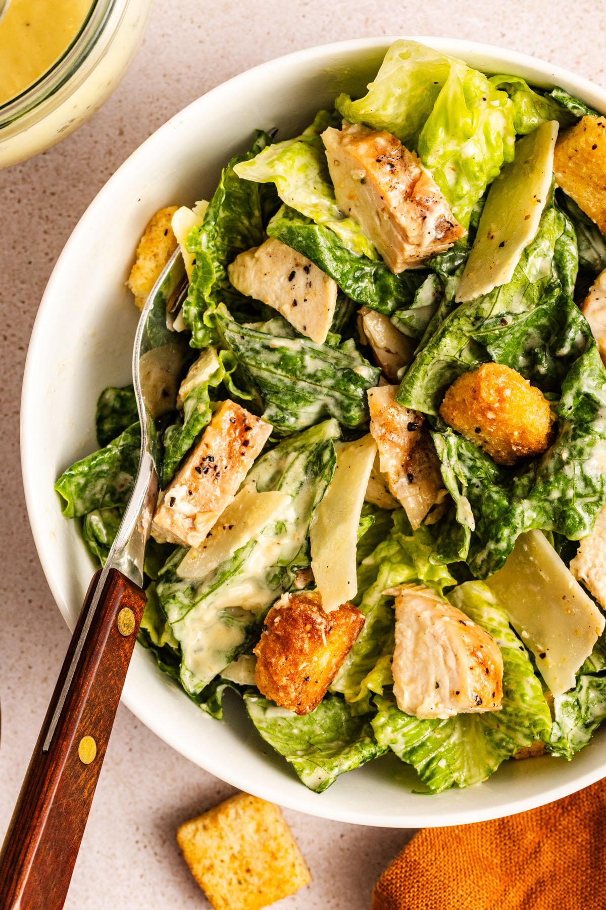 A bowl of chicken Caesar salad with a fork resting in the bowl.
