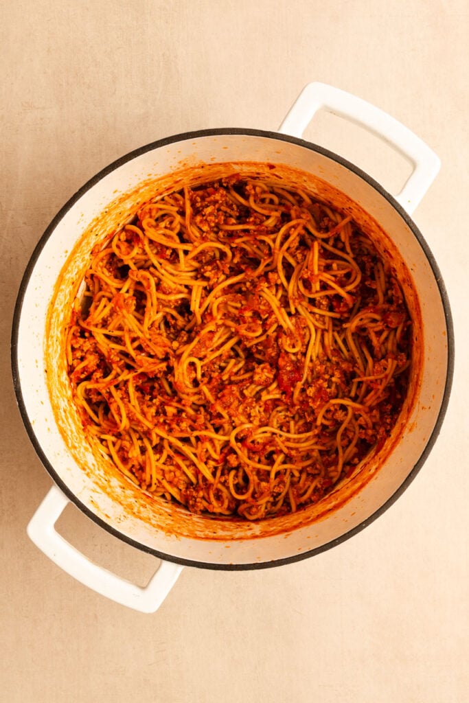 A one pot spaghetti dinner with turkey Bolognese sauce simmering in a white dutch oven, viewed from above.