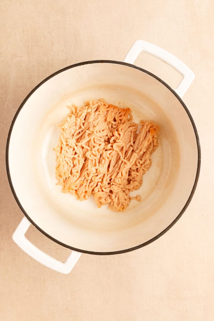 Raw ground meat in a white Dutch oven sitting on a light-colored surface.