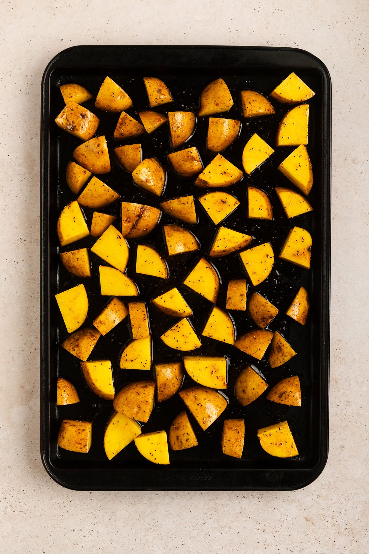 A baking tray with evenly spread, seasoned Yukon Gold potato chunks on a light-colored surface, ready to be roasted.