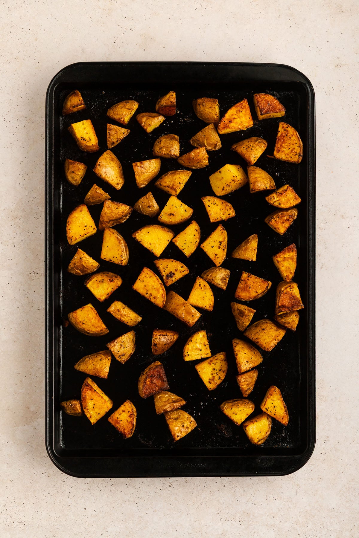 Crispy roasted Yukon Gold potato cubes on a black metal sheet pan.