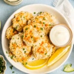A plate of baked fish cakes garnished with parsley, served with lemon wedges and a small bowl of dipping sauce; cucumber salad and sauce are nearby.