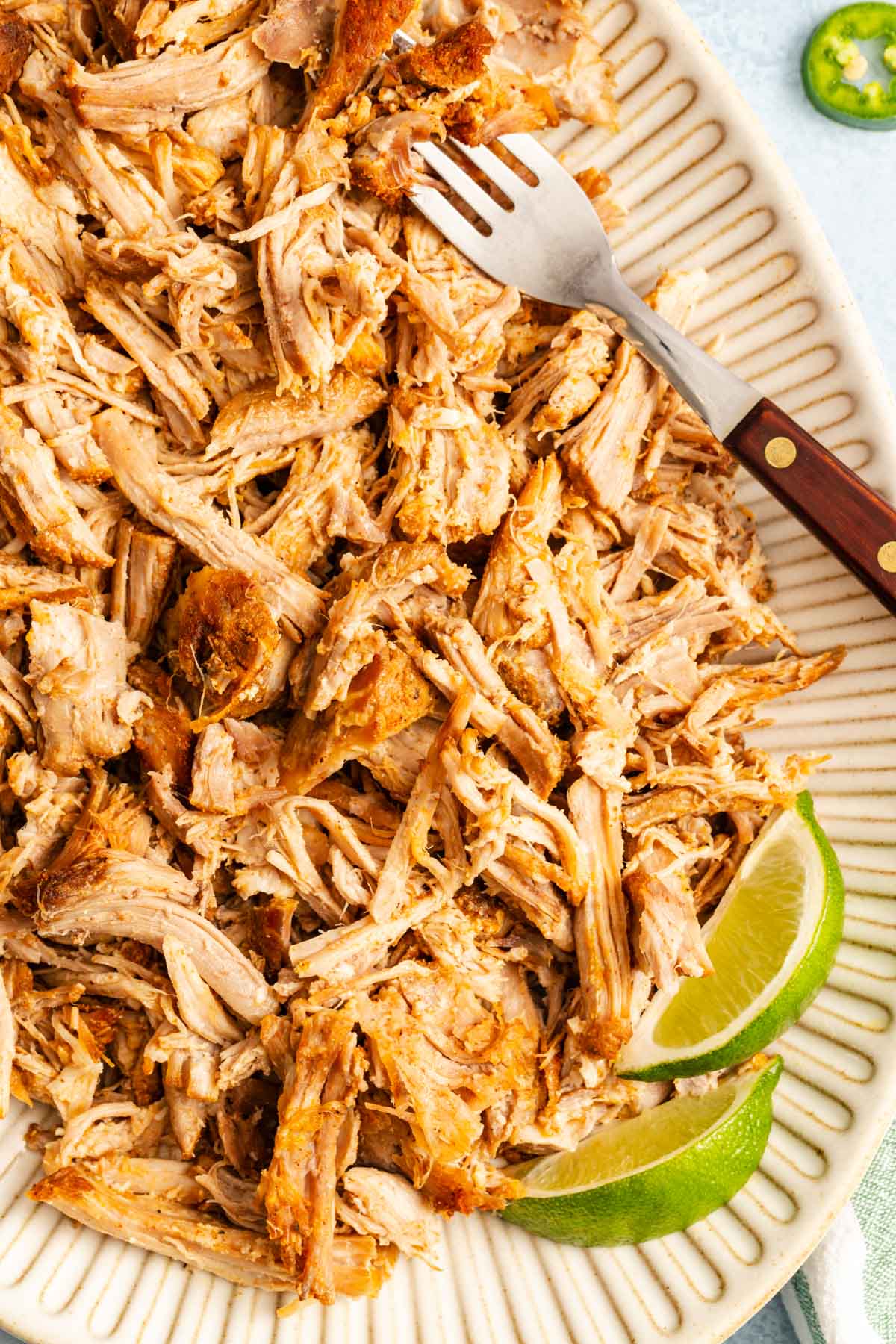 Shredded carnitas served over white rice on a plate with a serving fork and lime wedges.