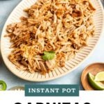 Oval platter filled with shredded pork carnitas, garnished with cilantro, lime wedges nearby, with part of an Instant Pot visible in the background.