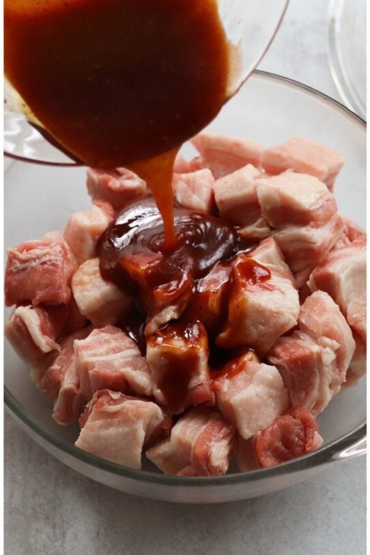 A bowl of raw cubed pork belly with a dark sauce being poured over the top.