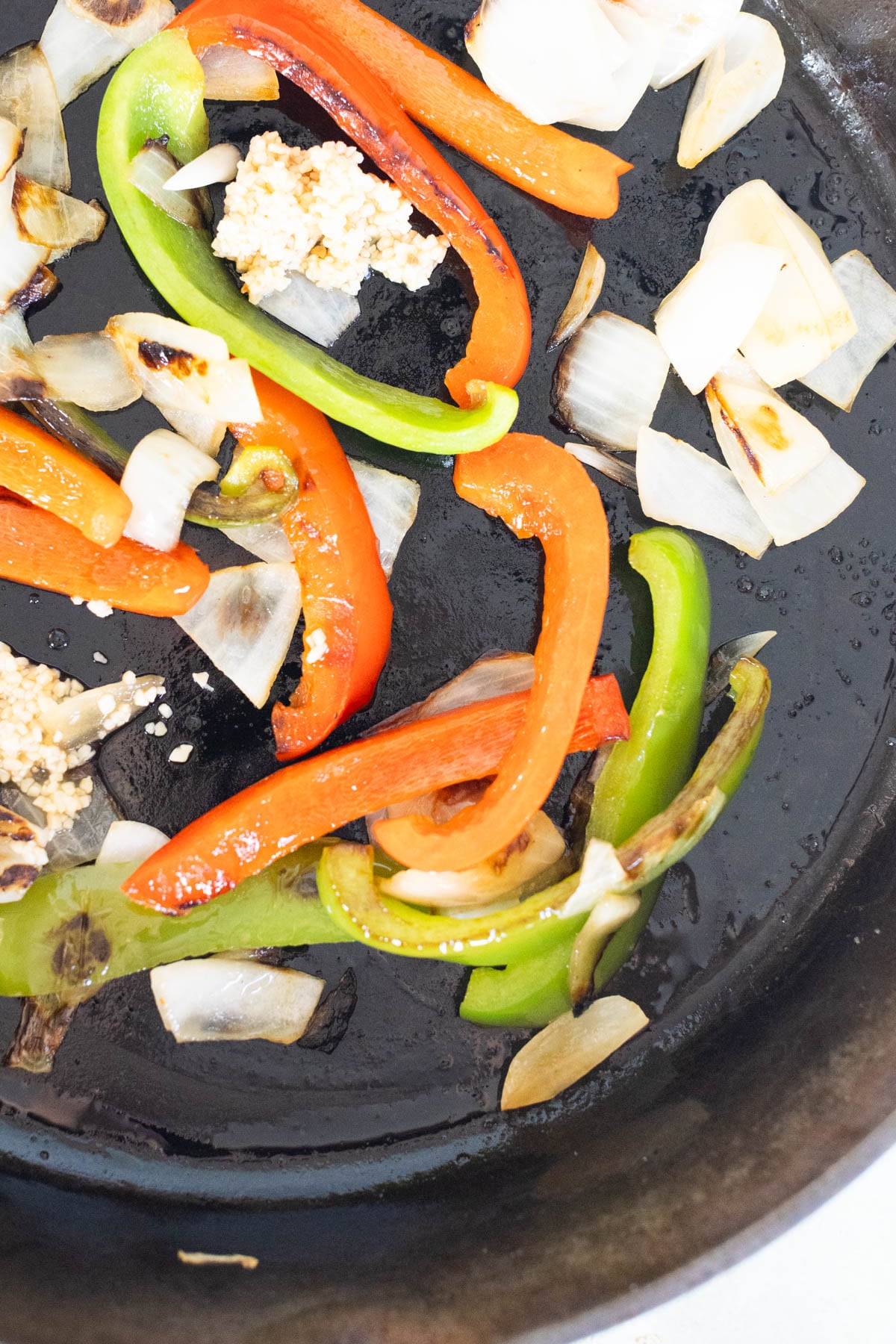 Sliced red and green bell peppers, chopped onions, and minced garlic cooking in a black skillet.