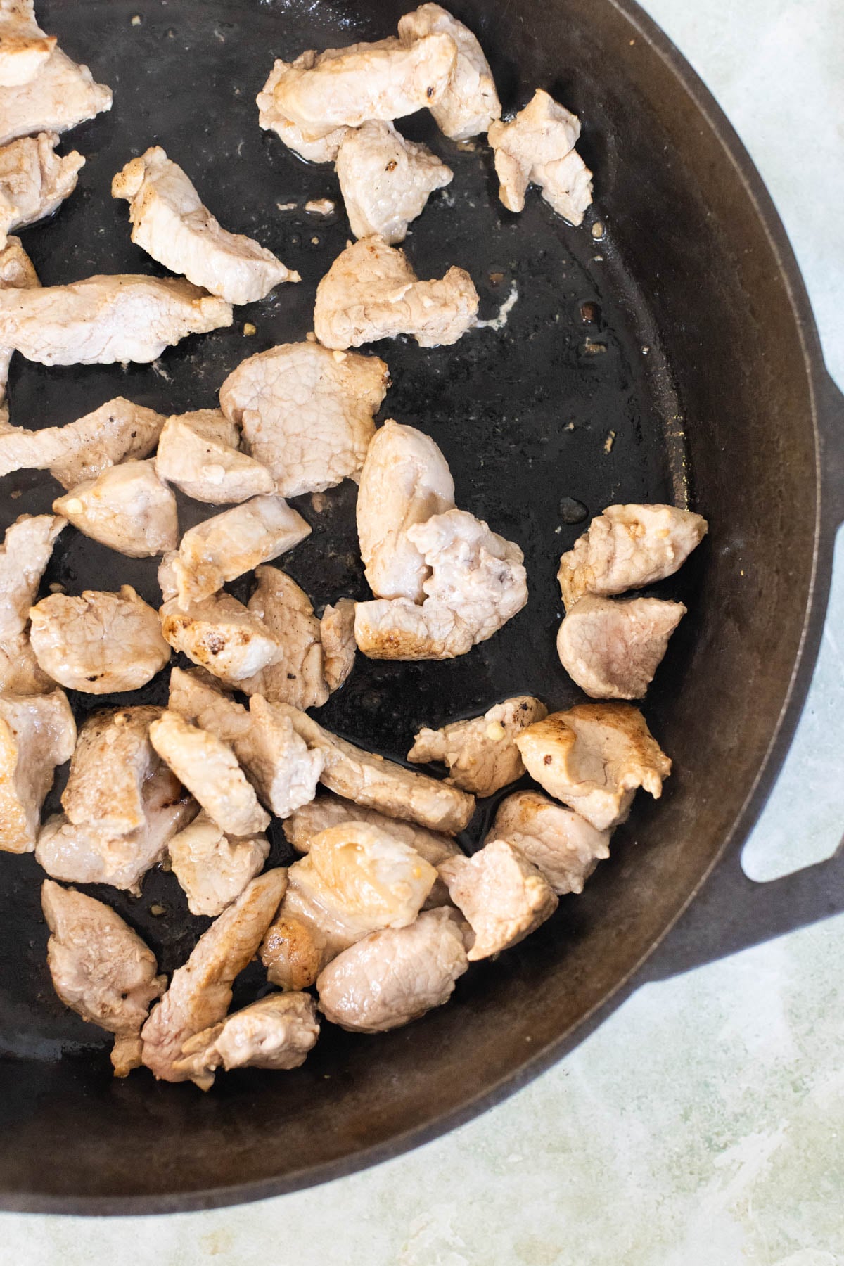Slices of cooked pork tenderloin in a black skillet, viewed from above.