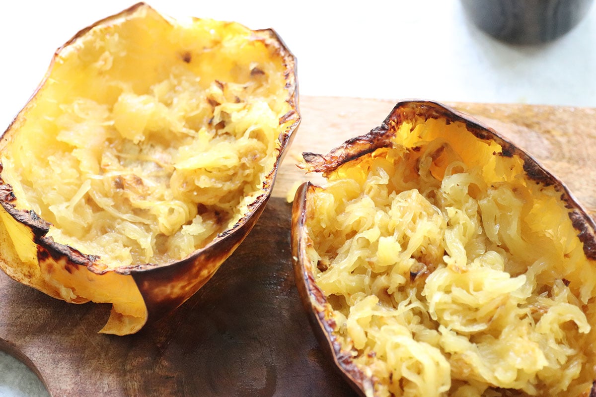 Two air fried spaghetti squash halves with stringy flesh inside, placed on a wooden surface.
