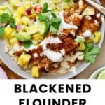 A plate of blackened flounder topped with pineapple salsa, avocado, cilantro, and a creamy sauce, served over rice, with a lime wedge on the side.