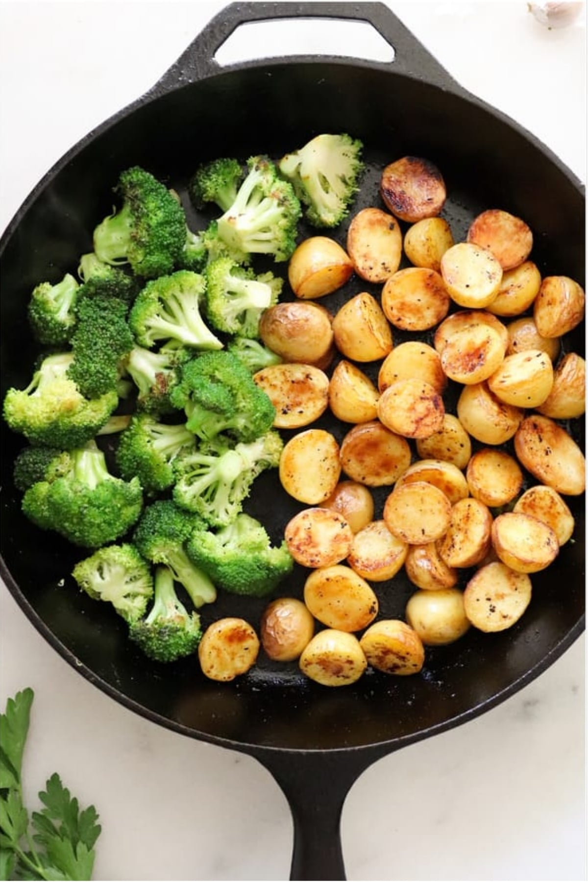 A cast iron skillet with sautéed broccoli florets on one side and golden-brown roasted baby potatoes on the other side.