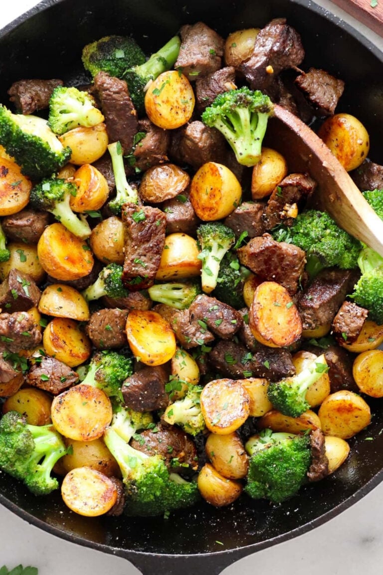 A skillet filled with cooked steak pieces, halved golden potatoes, and broccoli florets, all mixed together with herbs.