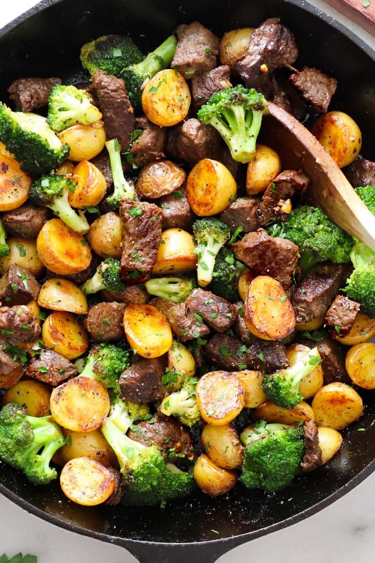 A skillet filled with cooked steak pieces, halved golden potatoes, and broccoli florets, all mixed together with herbs.