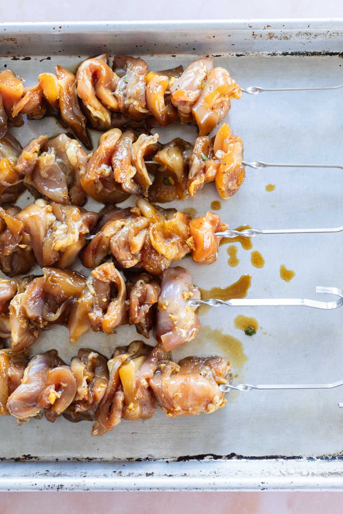 Teriyaki chicken skewers arranged on a baking sheet, ready for grilling.