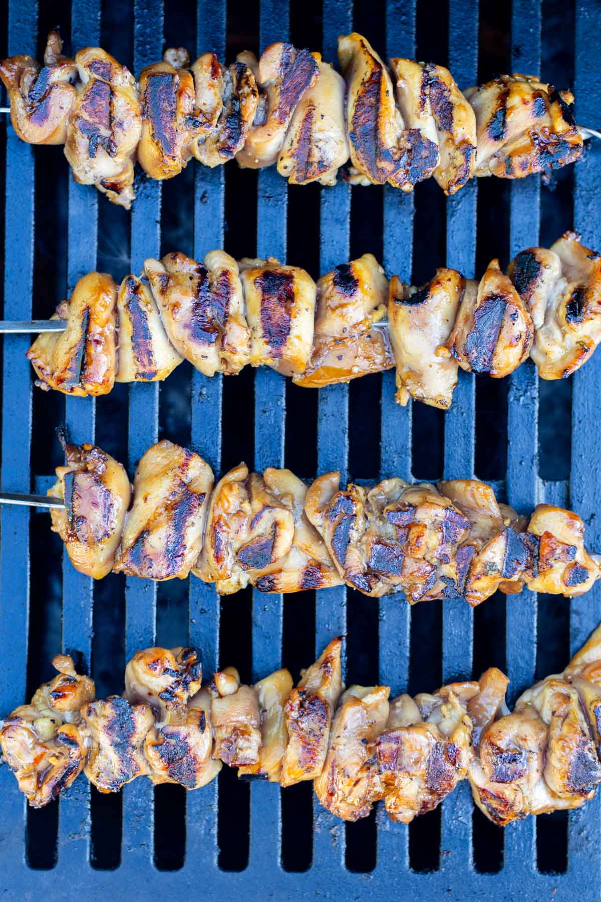 Four grilled chicken skewers with char marks are arranged on the metal grates.