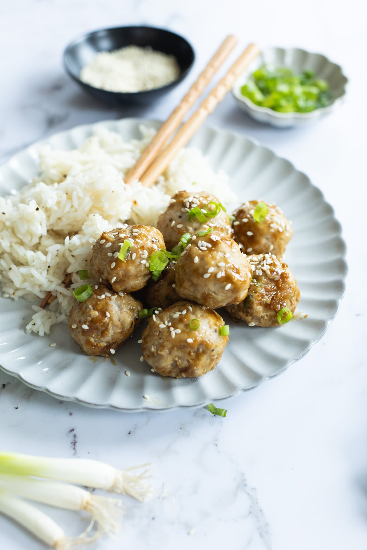 A plate of white rice and sesame-topped meatballs garnished with chopped green onion, with chopsticks resting on the plate.