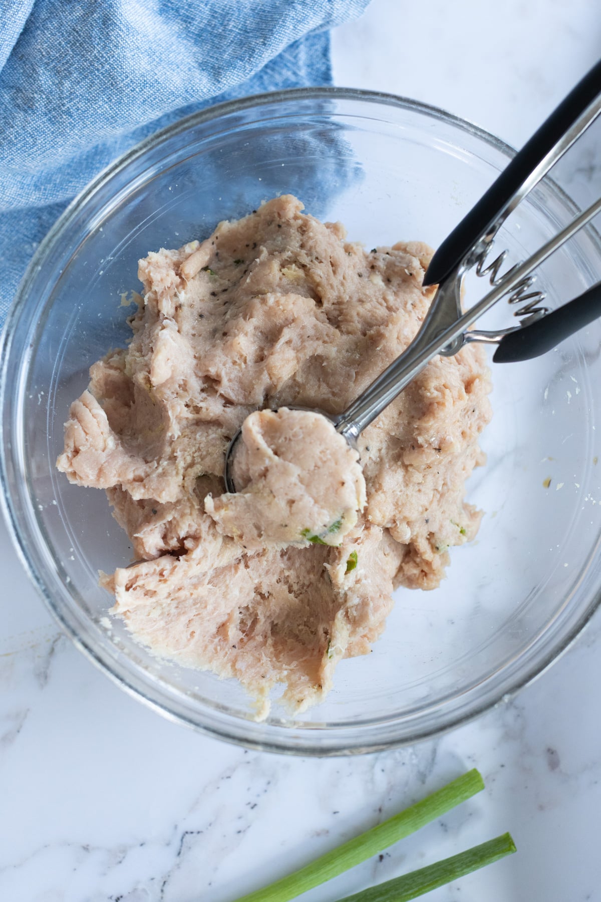 Glass bowl with raw meatball mixture being scooped out.