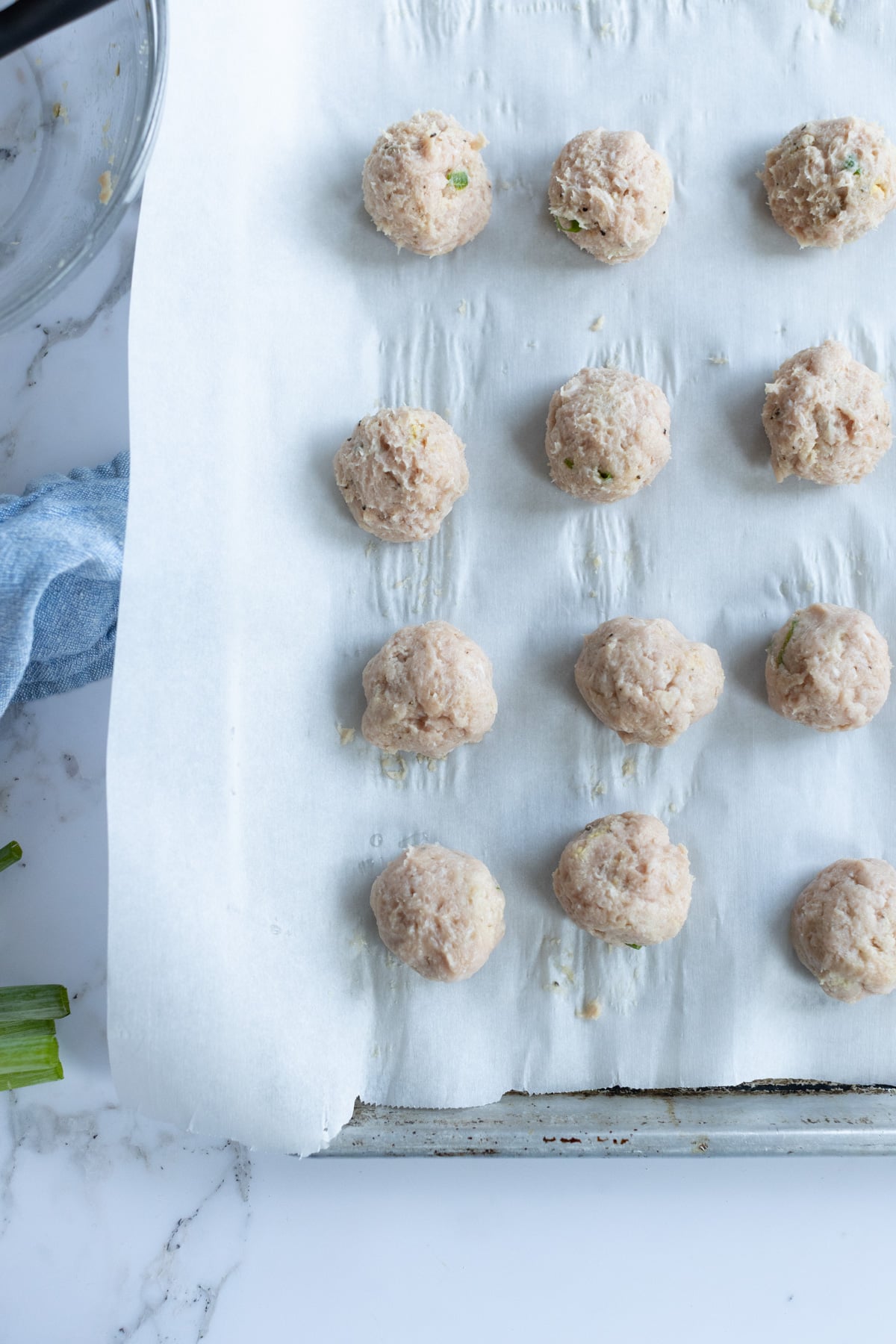 Unbaked teriyaki meatballs arranged in rows on a parchment-lined baking sheet, ready to be baked.