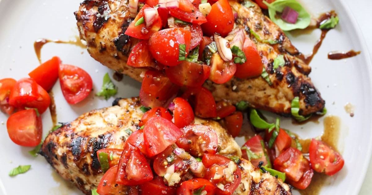 Grilled chicken breasts topped with chopped cherry tomatoes, fresh basil, and minced garlic on a white plate.