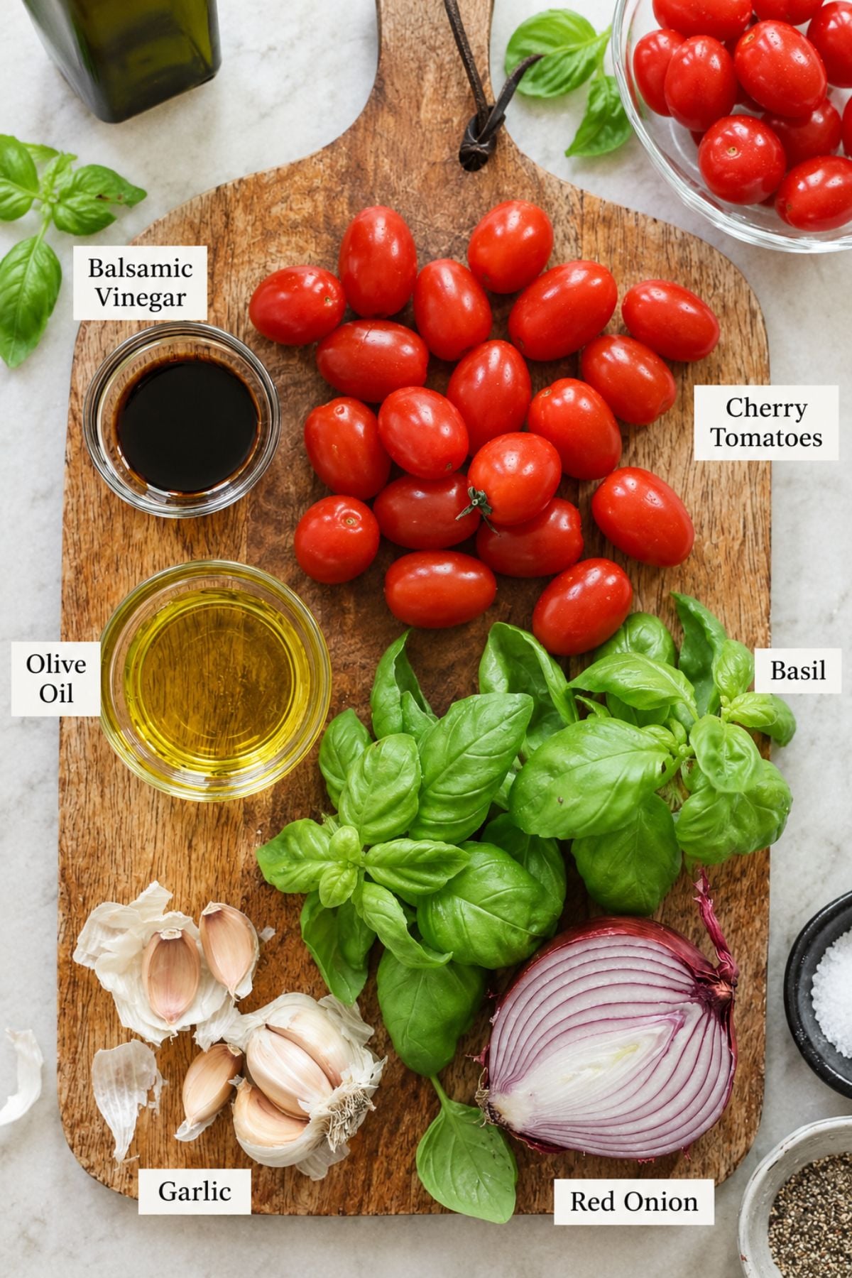 Ingredients for a tomato basil salad arranged on a wooden board: cherry tomatoes, basil, red onion, garlic, olive oil, and balsamic vinegar—perfect flavors to pair with bruschetta chicken.
