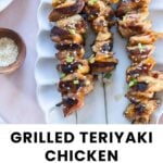 Three grilled teriyaki chicken skewers garnished with green onions and sesame seeds are arranged on a white plate.