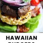 A Hawaiian burger with lettuce, grilled pineapple, bacon, beef patty, red onion, sauce, and cilantro, served on parchment with cherry tomatoes in the background.