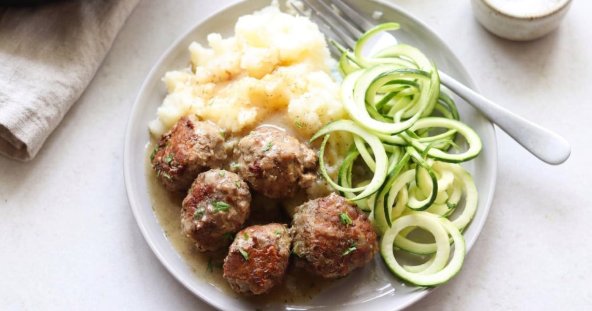 A plate with Swedish meatballs in sauce, mashed potatoes, and spiralized zucchini, served with a fork.