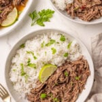 A bowl of shredded beef and white rice garnished with chopped parsley and a lime wedge, with a similar plate and a serving dish nearby.