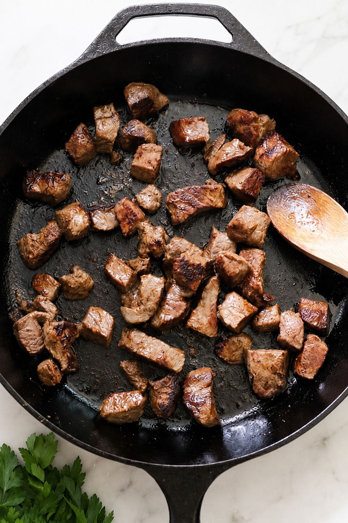 Cubed beef is searing in a black cast iron skillet.