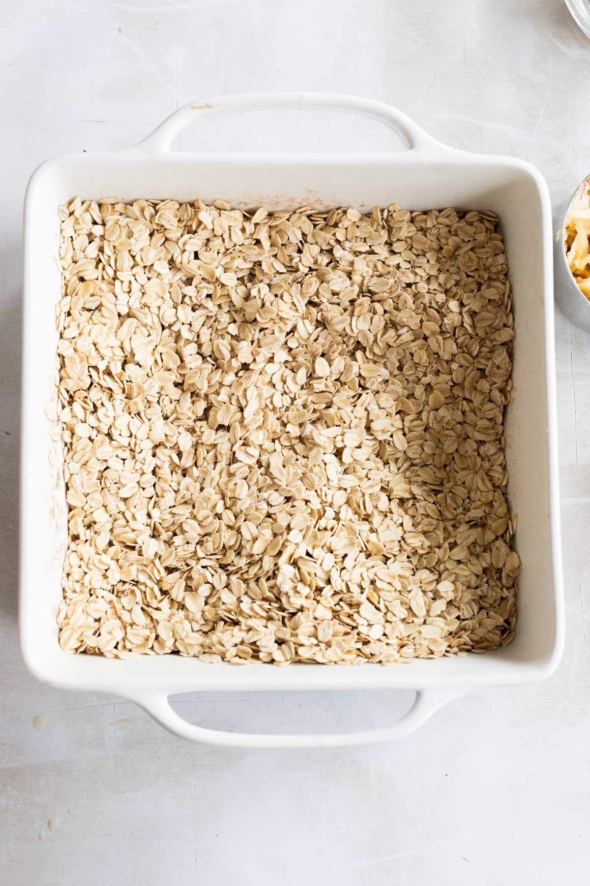 Square white baking dish filled with an even layer of uncooked rolled oats.
