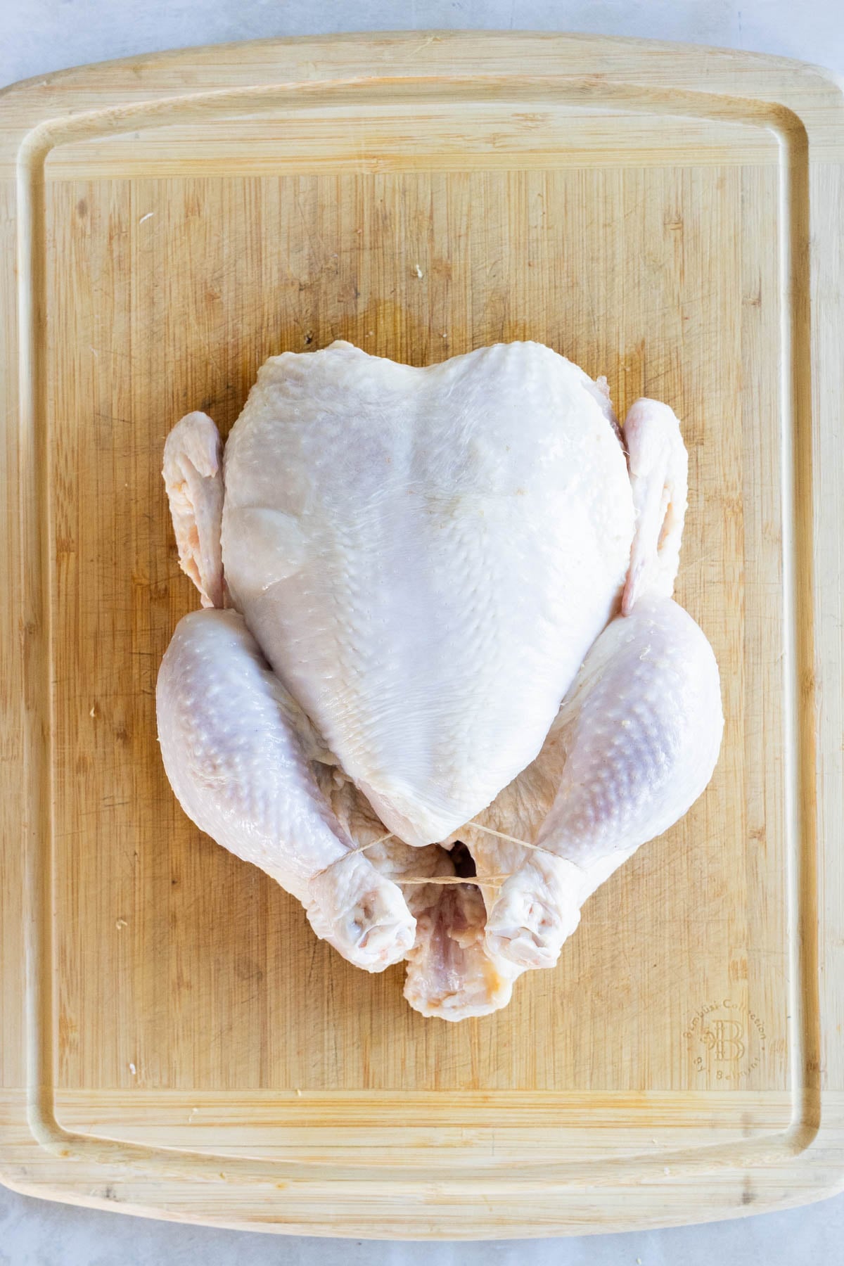 Raw whole chicken placed on a wooden cutting board, viewed from above.