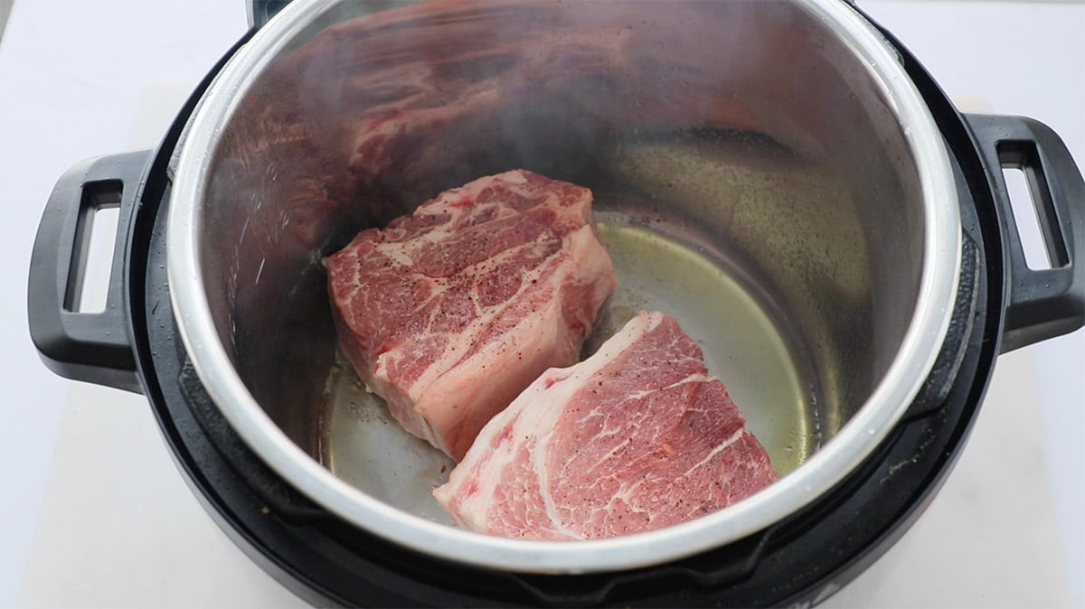 Two raw pieces of pork butt in an Instant Pot.