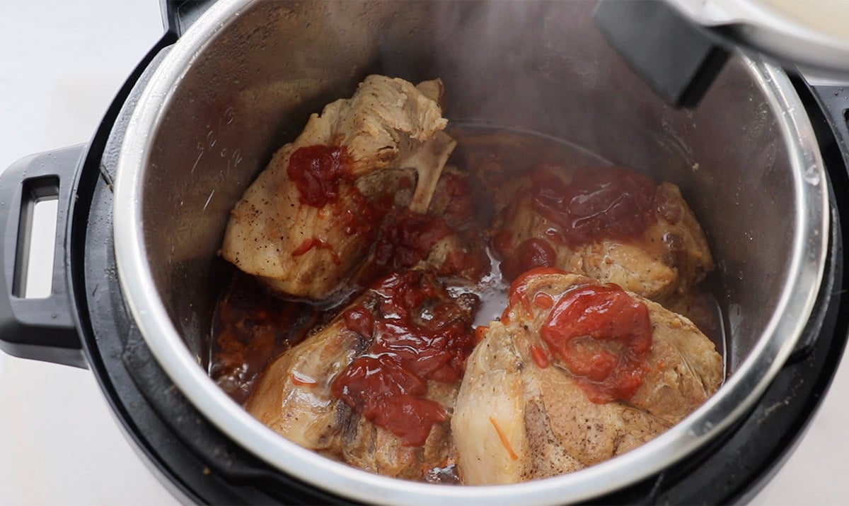 Four pieces of cooked meat and BBQ sauce sit inside an electric pressure cooker.