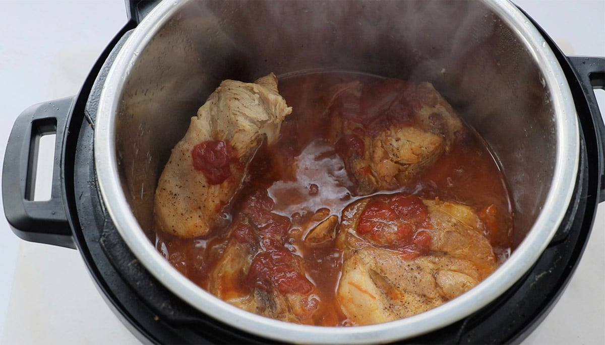 Pork shoulder cooking in an Instant Pot. Steam is visible, and the meat is partially submerged in BBQ sauce.