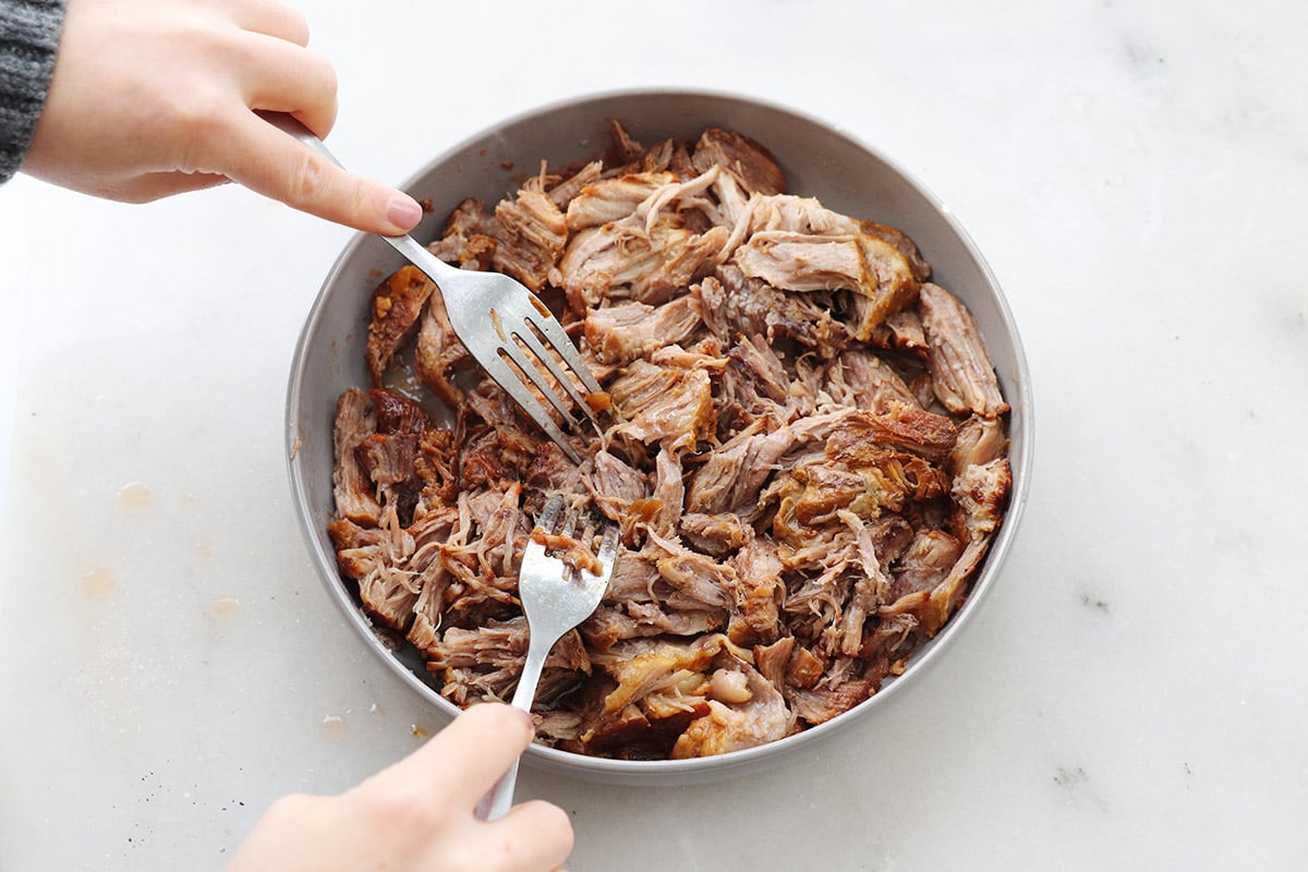 Two hands use forks to shred pulled pork in an Instant Pot.