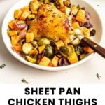 A sheet pan dinner with roasted chicken thigh, Brussels sprouts, sweet potatoes, and red onions on a white plate with a fork.