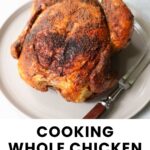 A cooked whole chicken sits on a plate with a serving fork and knife beside it. Text below reads, “Cooking Whole Chicken in the Air Fryer. Cook at Home Mom.”.