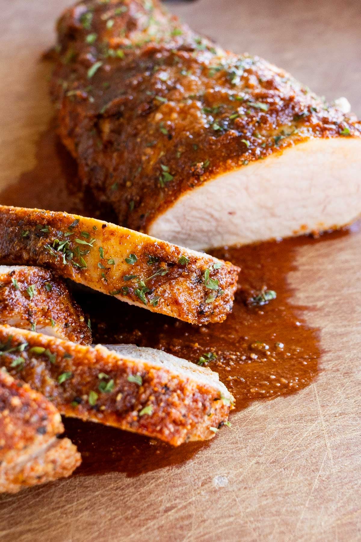 A seasoned, sliced pork tenderloin on a wooden cutting board with juices.