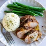 Sliced seasoned pork tenderloin served with mashed potatoes and green beans on a plate.