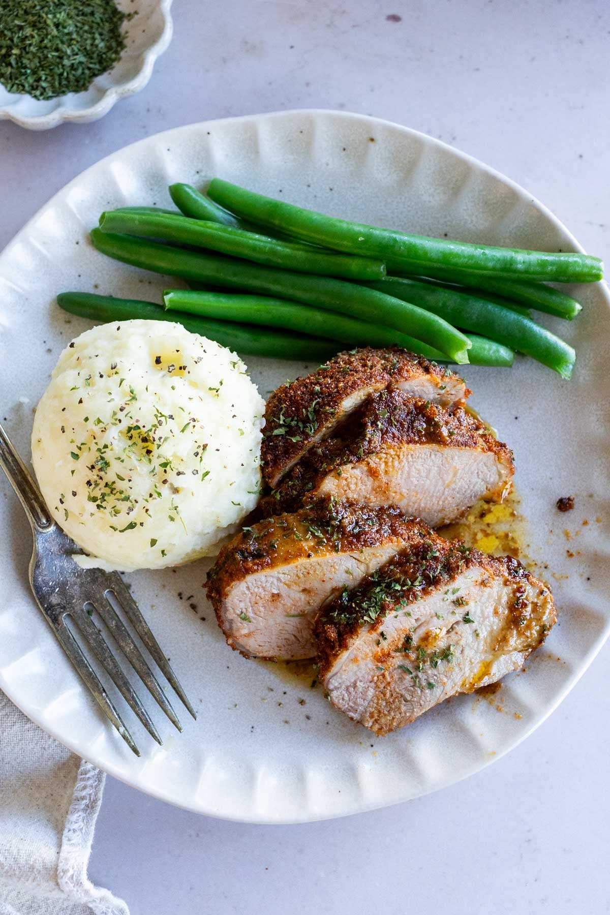 Sliced seasoned pork tenderloin served with mashed potatoes and green beans on a plate.